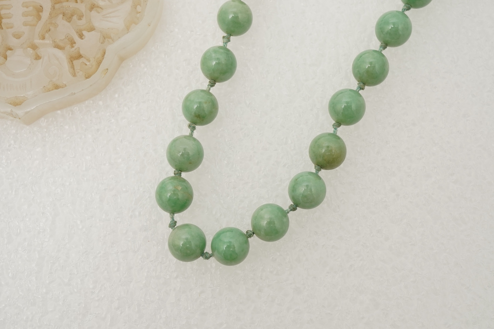 A Chinese jade ‘spirit lock’ plaque, a jadeite bead necklace and a blue quartz bead necklace, 20th century